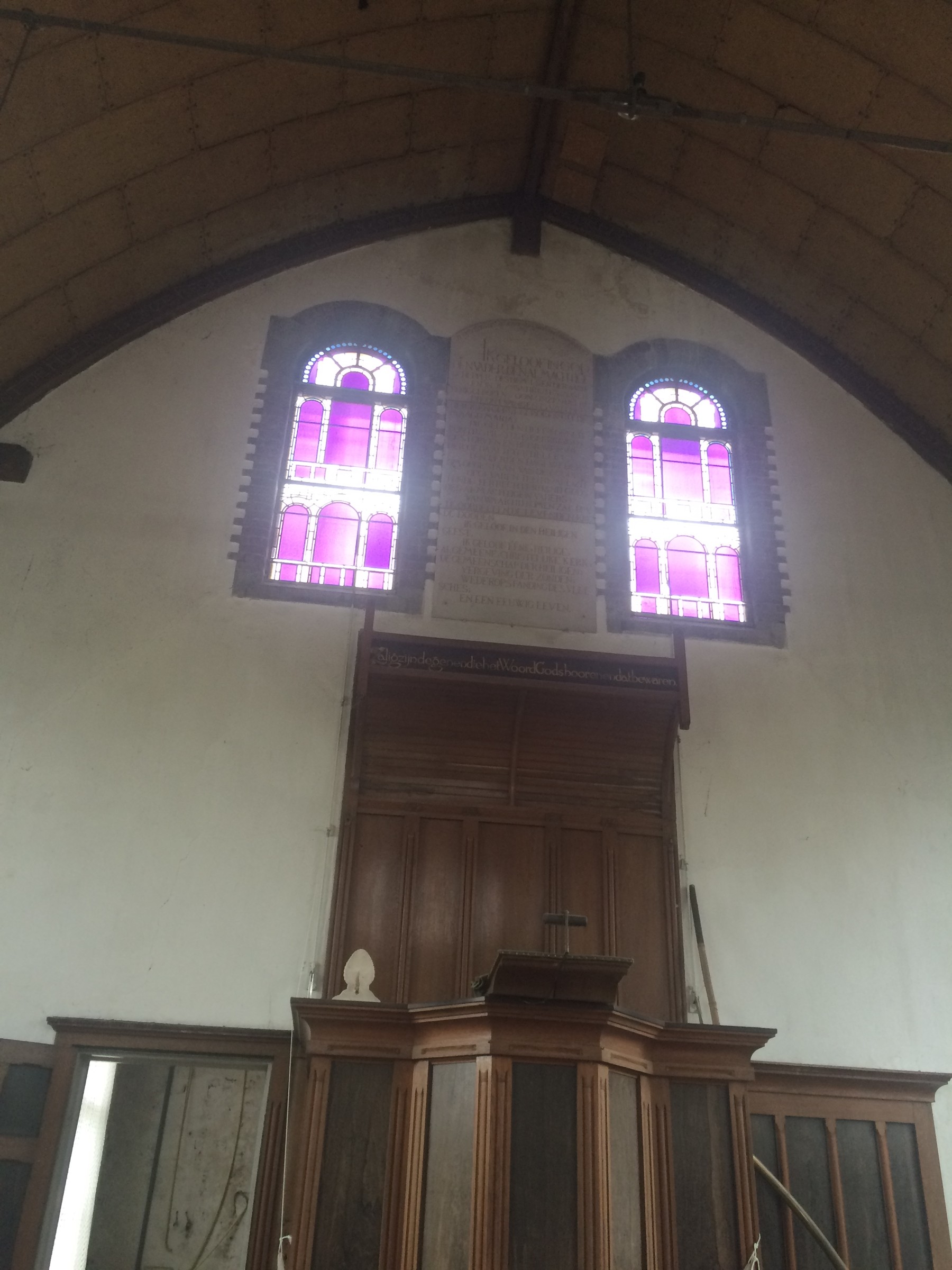 Een stil kerkinterieur, verlicht door roze en paarse glas-in-loodramen.